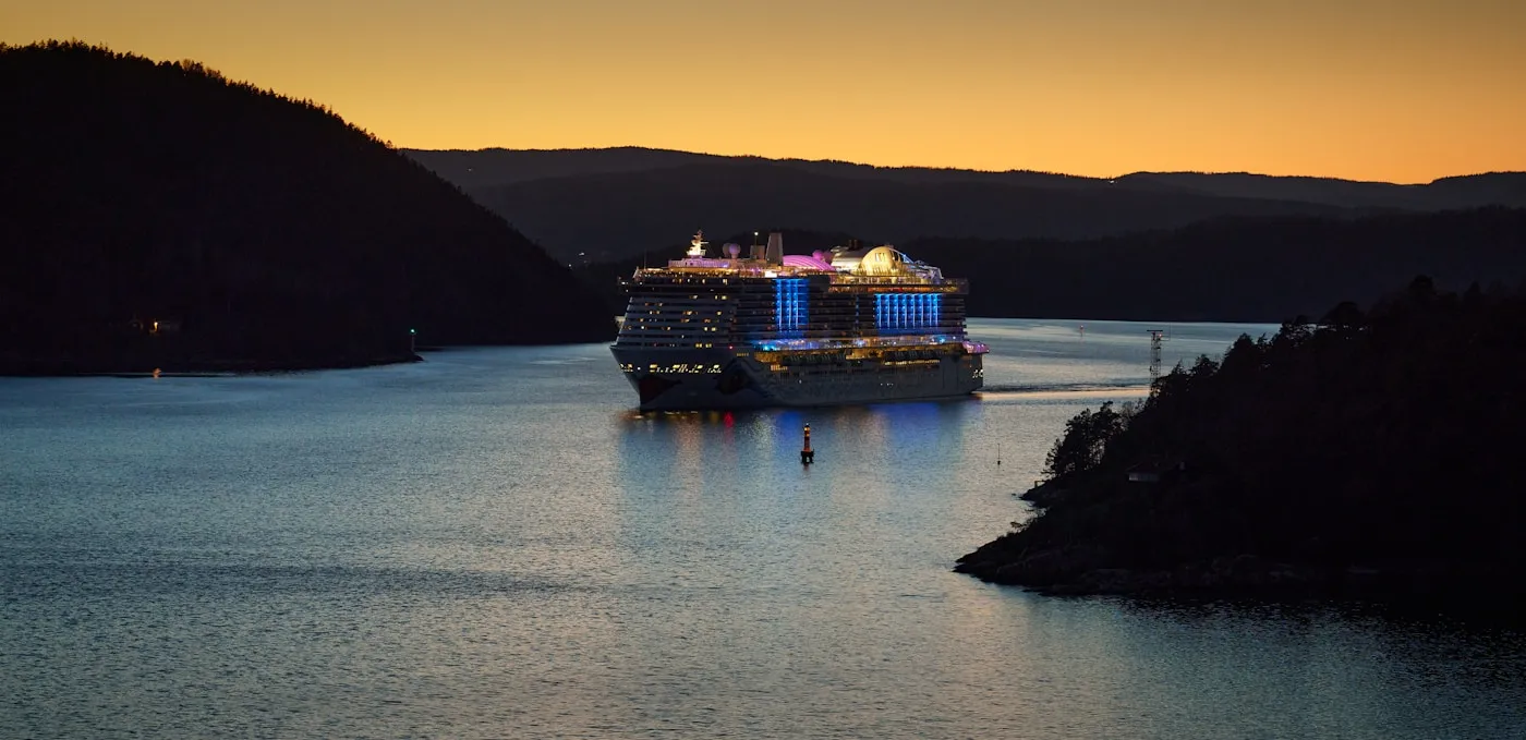 Cruise ship sailing through a Norwegian fjord at sunset